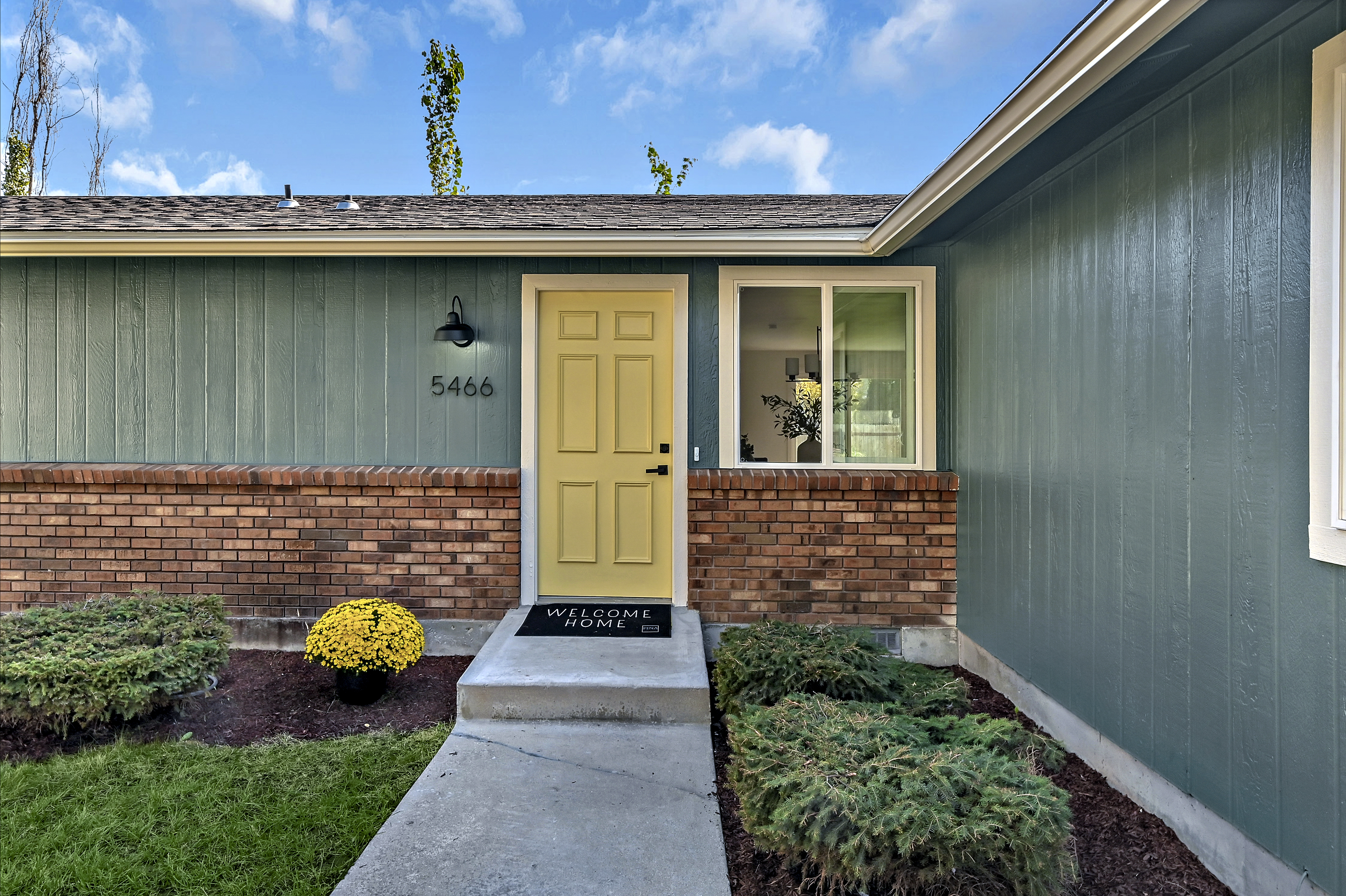 Millstream Front Door Welcome home mat sits on front step of green house with yellow door