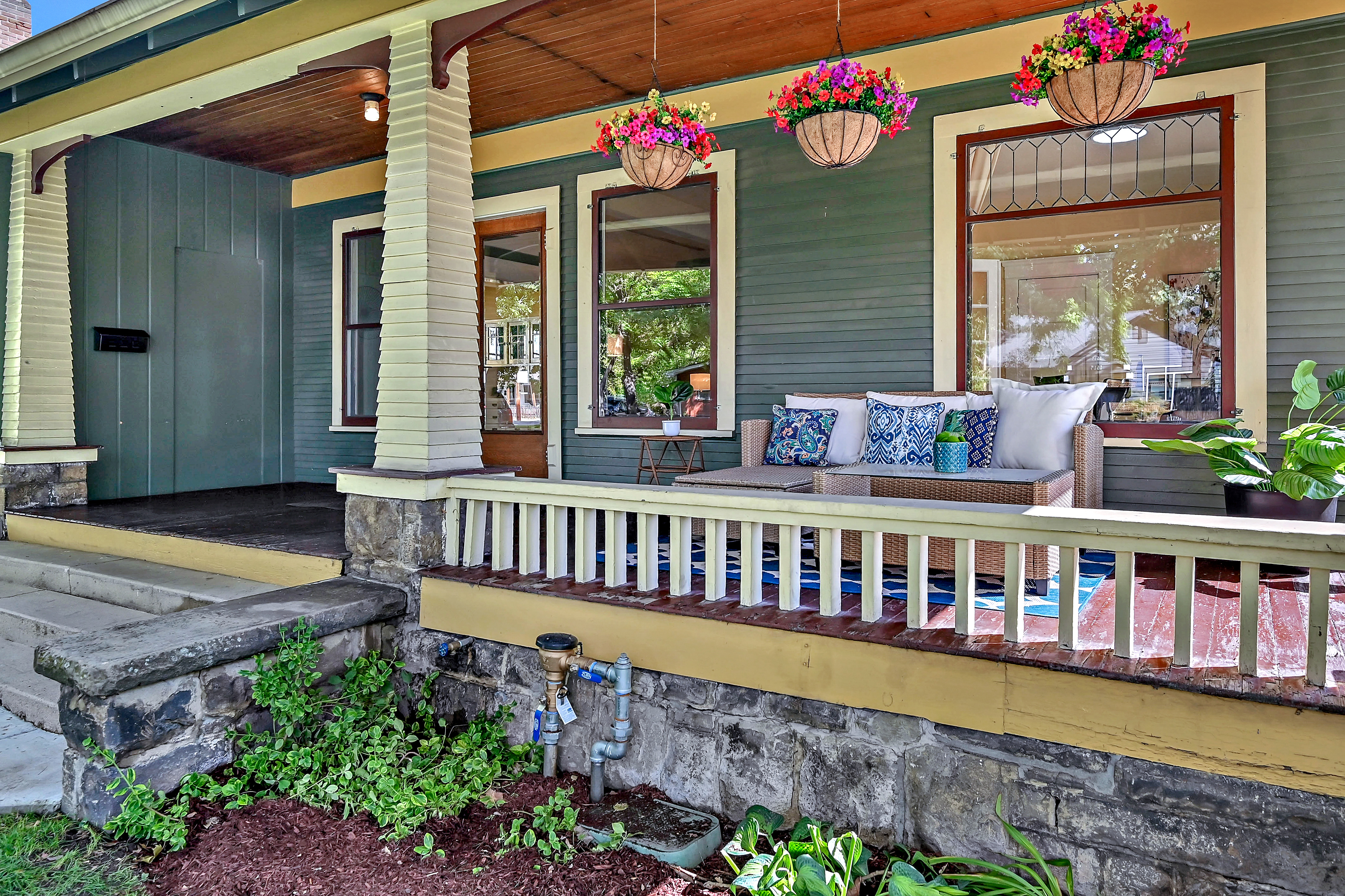 Craftsman style covered front porch with blue couch and colorful handing flower pots