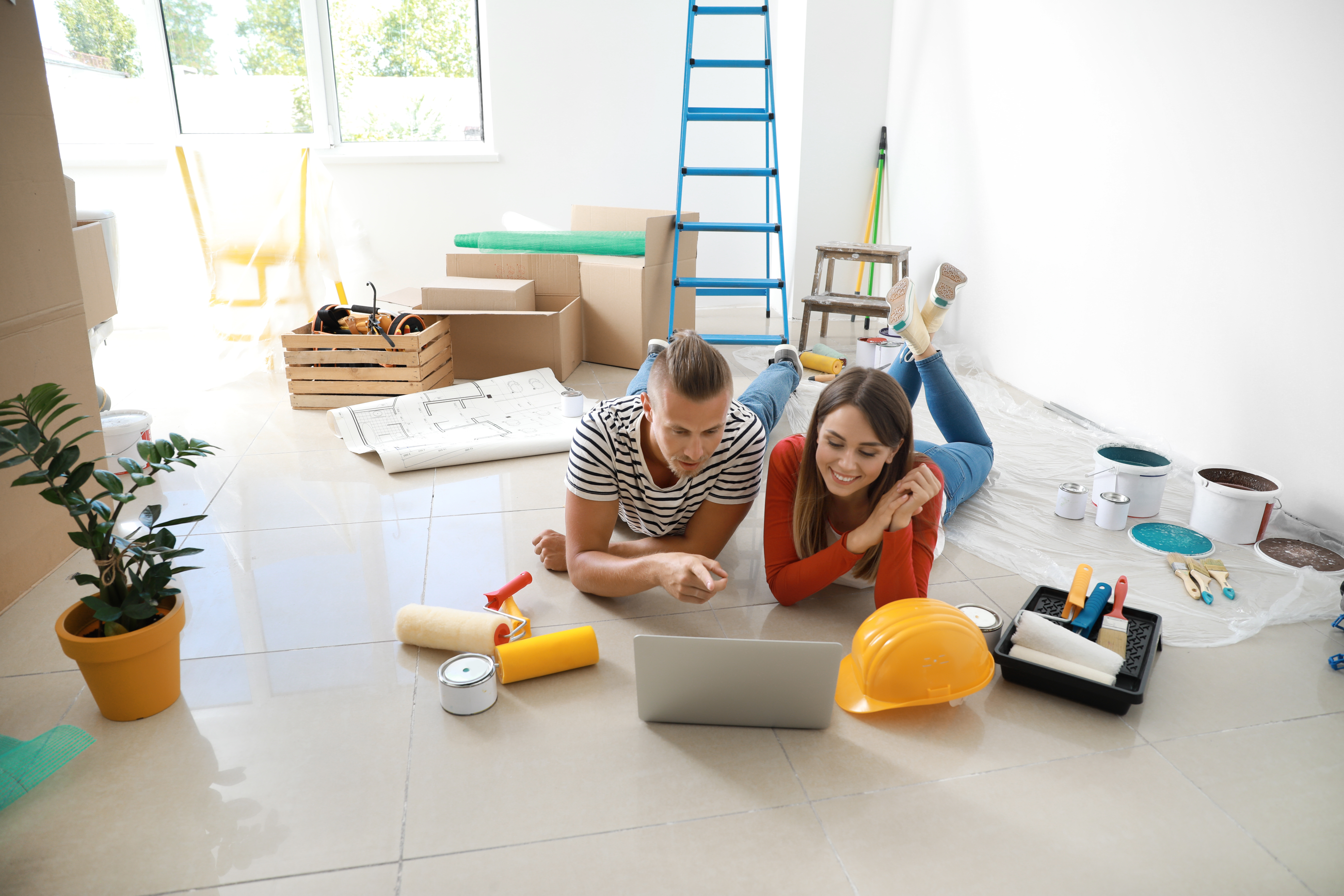 Man and woman surrounded by construction materials while sitting on floor.