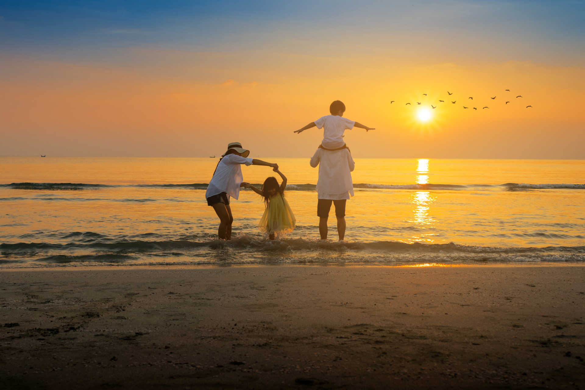  A family of four standing on the beach, silhouetted against a colorful sunset sky.