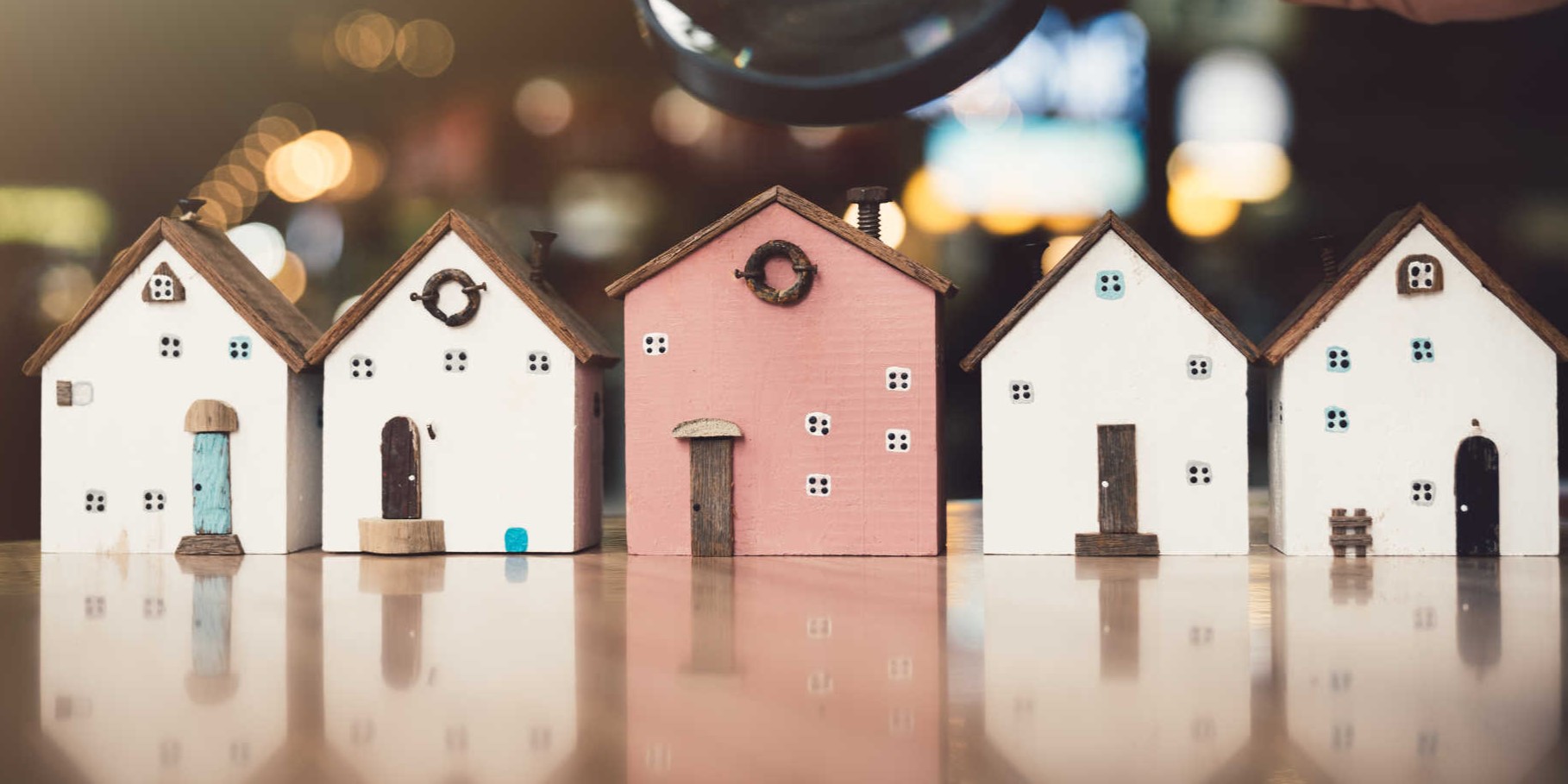 A person examines a tiny house closely with a magnifying glass, showcasing curiosity and attention to detail.