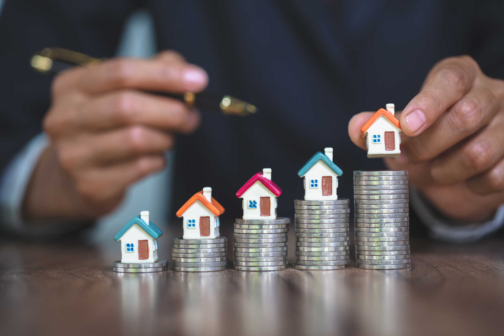 A man holds a stack of coins topped with miniature houses