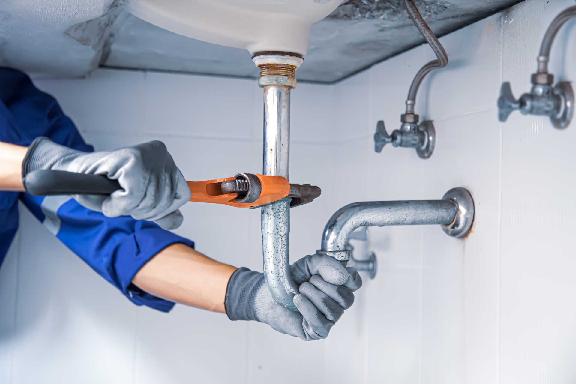  A plumber adjusts a sink faucet, surrounded by tools, demonstrating expertise in fixing plumbing issues with care.