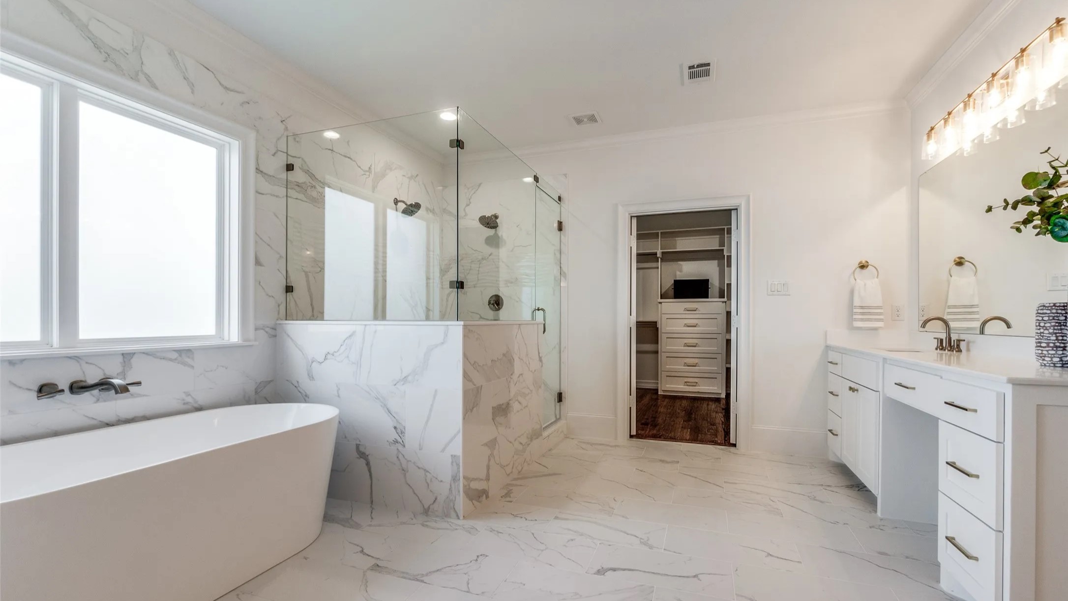 A spacious white bathroom featuring elegant marble flooring and a luxurious bathtub, creating a serene atmosphere.