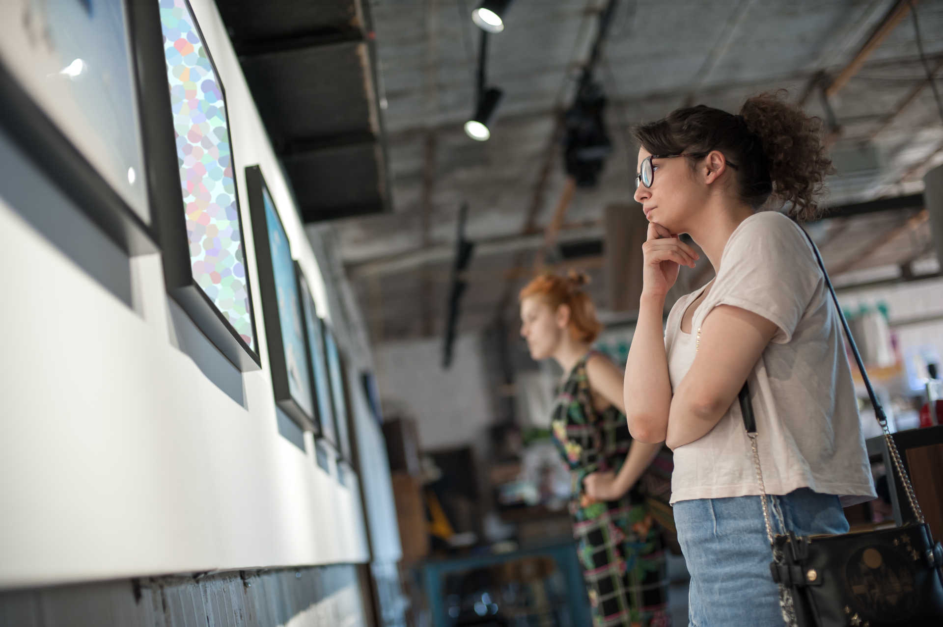 A woman gazes thoughtfully at a piece of art displayed in a contemporary art gallery, surrounded by vibrant colors.