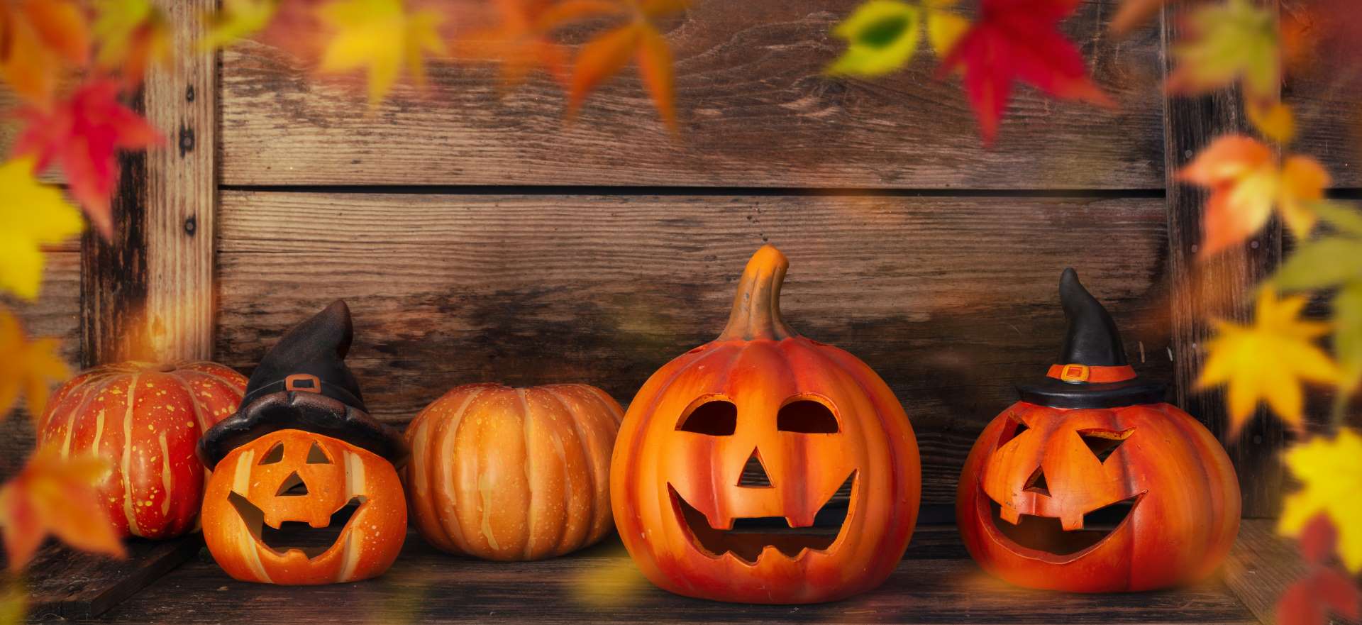 A wooden shelf adorned with Halloween pumpkins and scattered autumn leaves, creating a festive seasonal display.