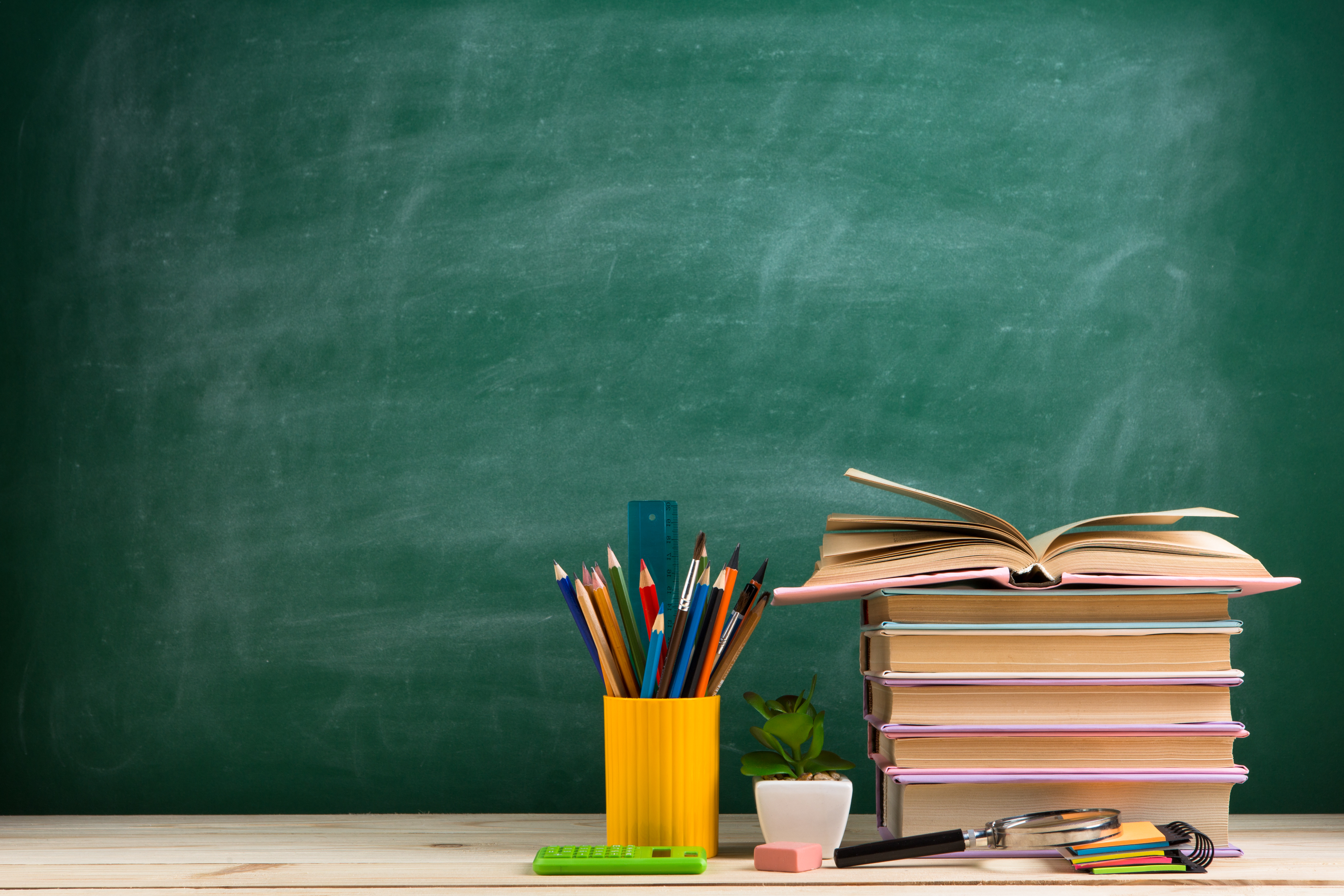 School supplies arranged on a wooden table, with a chalkboard in the background, creating an educational atmosphere.