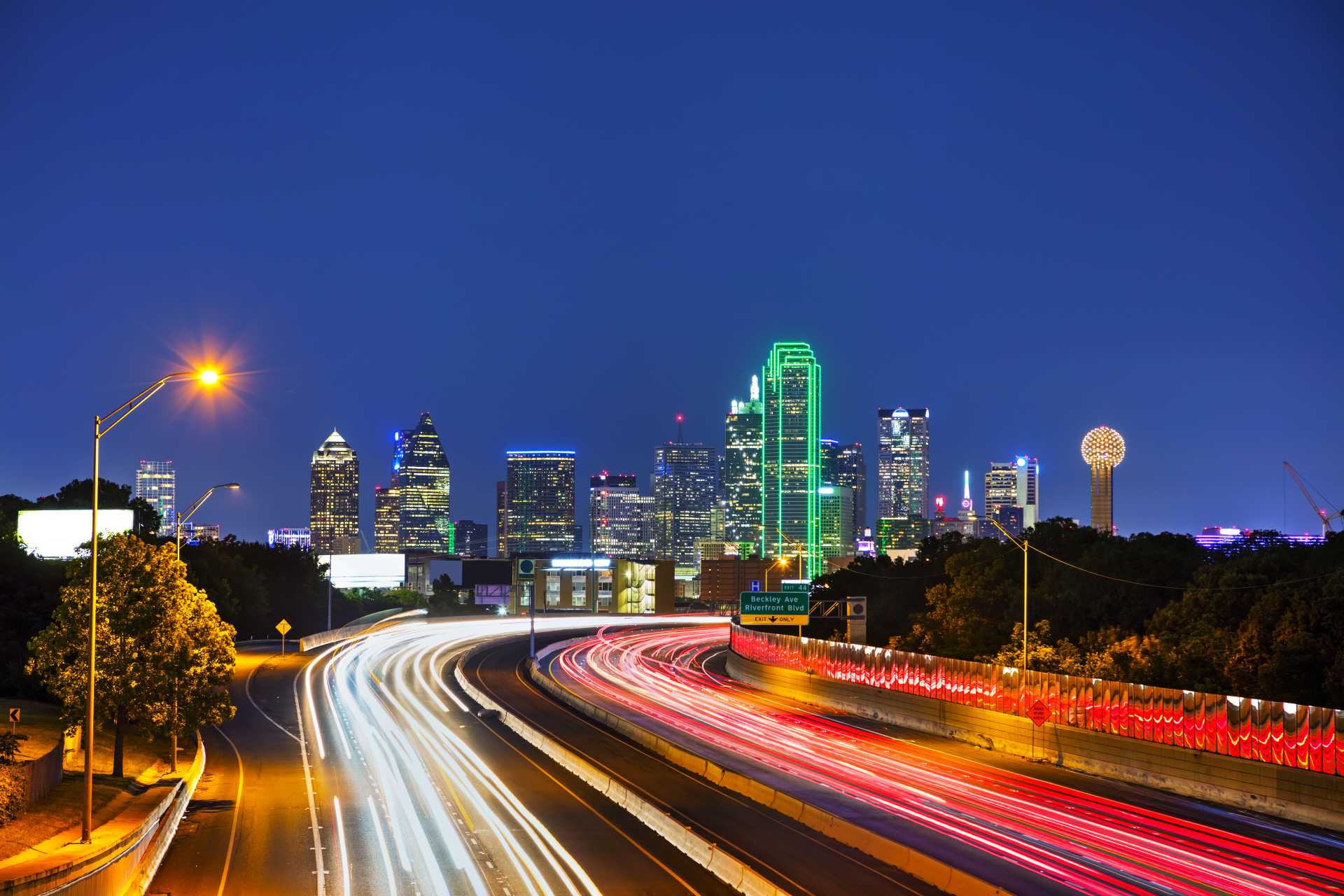 Night view of the Dallas skyline illuminated, with vibrant traffic flowing along the highway below.