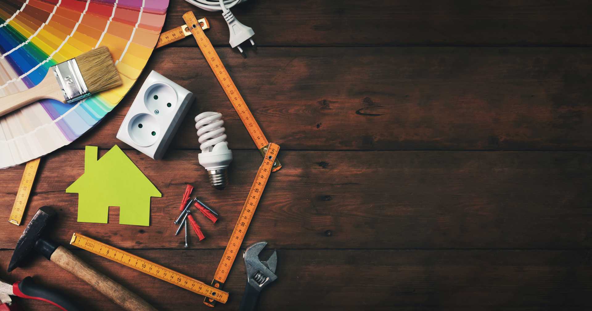 A variety of home improvement tools and supplies arranged on a wooden table, showcasing items like hammers, screws, and paint.