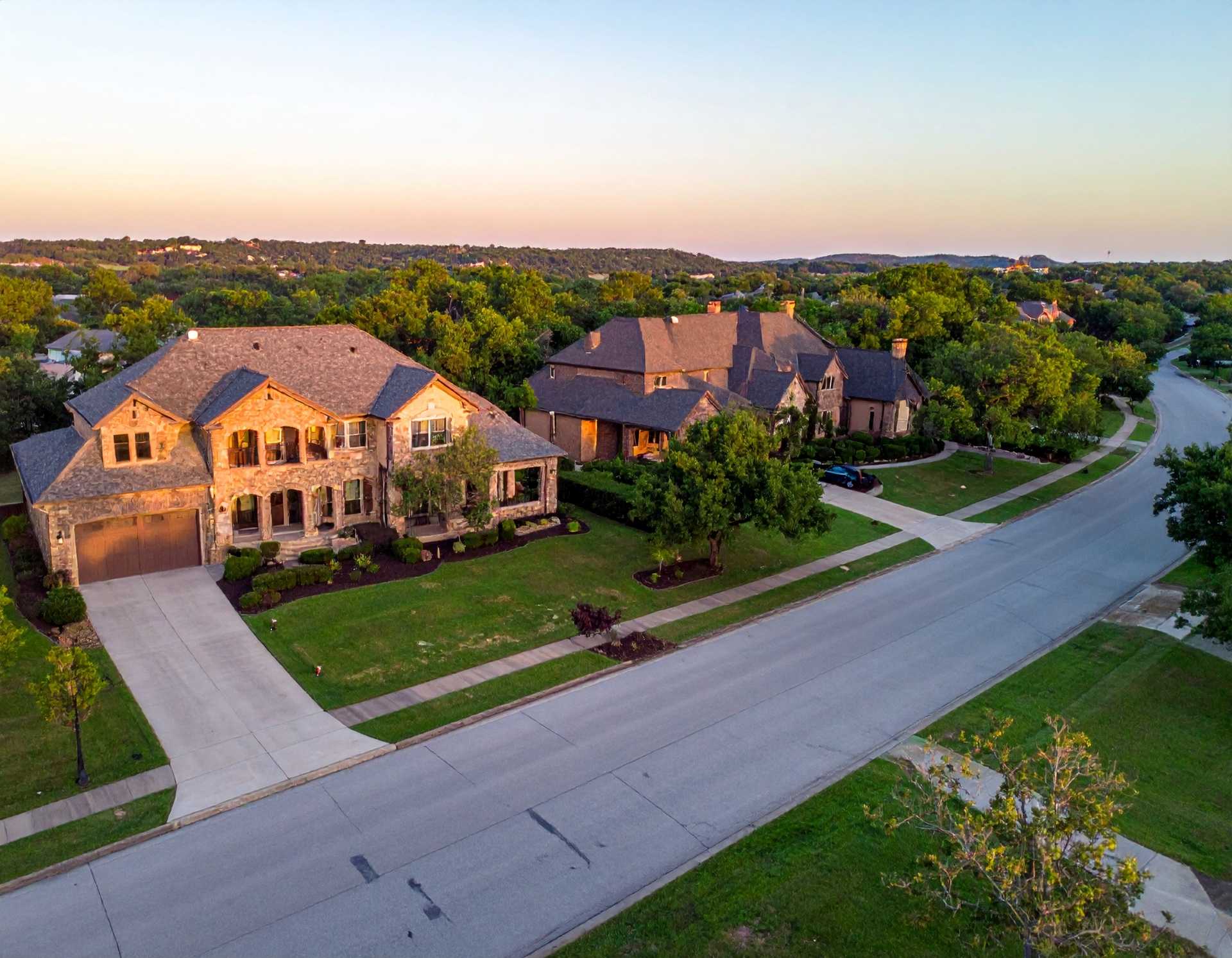 Bird's-eye view of a large home in a suburban setting, featuring well-kept gardens and nearby houses in the neighborhood.