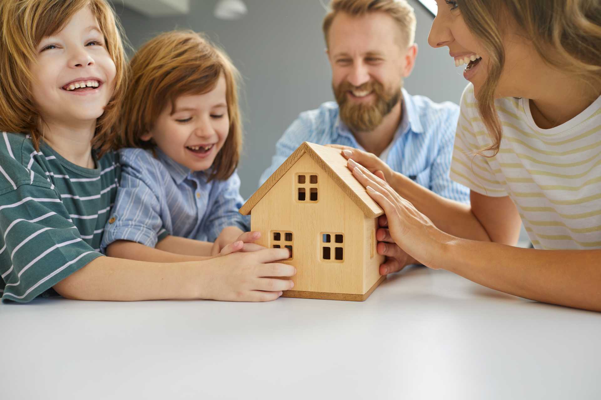 Happy family exploring fall market opportunities while planning their new home purchase, symbolized by a wooden house model on a table.