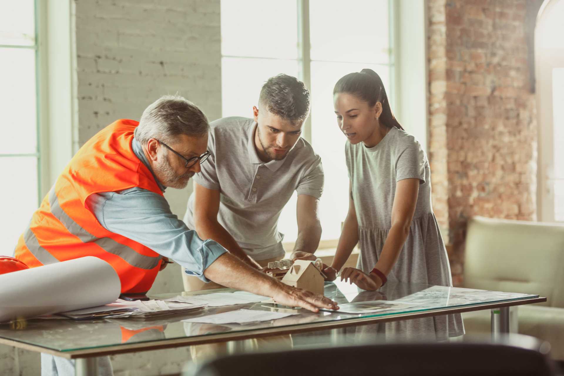 Young couple reviewing architectural blueprints with contractor in orange safety vest - Don't Fall for Builder Rate Traps when planning your custom home construction project