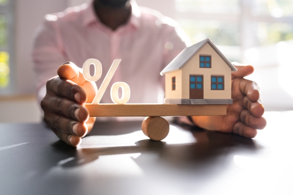 House model balanced with an interest rate percentage symbol illustrating how North Texas mortgage rates affect home affordability and monthly mortgage payments for homebuyers.
