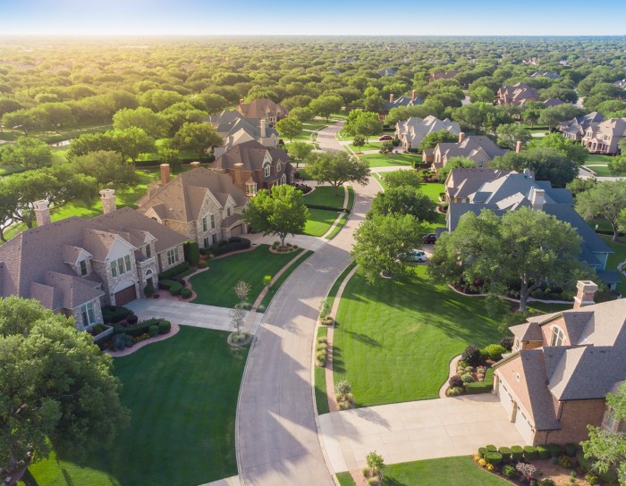 Aerial view of a tree-lined Dallas-area neighborhood with brick and stone homes, green lawns, and a curving street at sunset