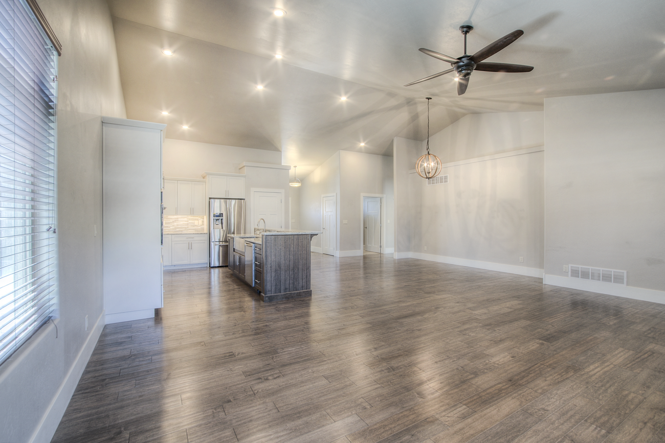 open concept living room/kitchen with white cupboards, stainless steel appliances, and vaulted ceiling. 