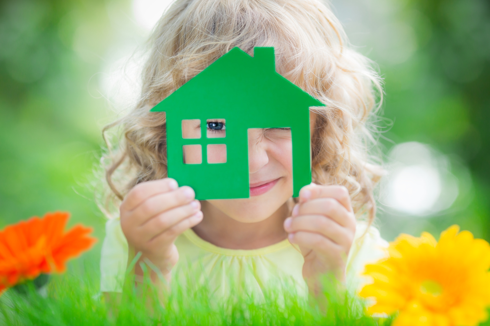 Small girl looking through green paper house with flowers surround