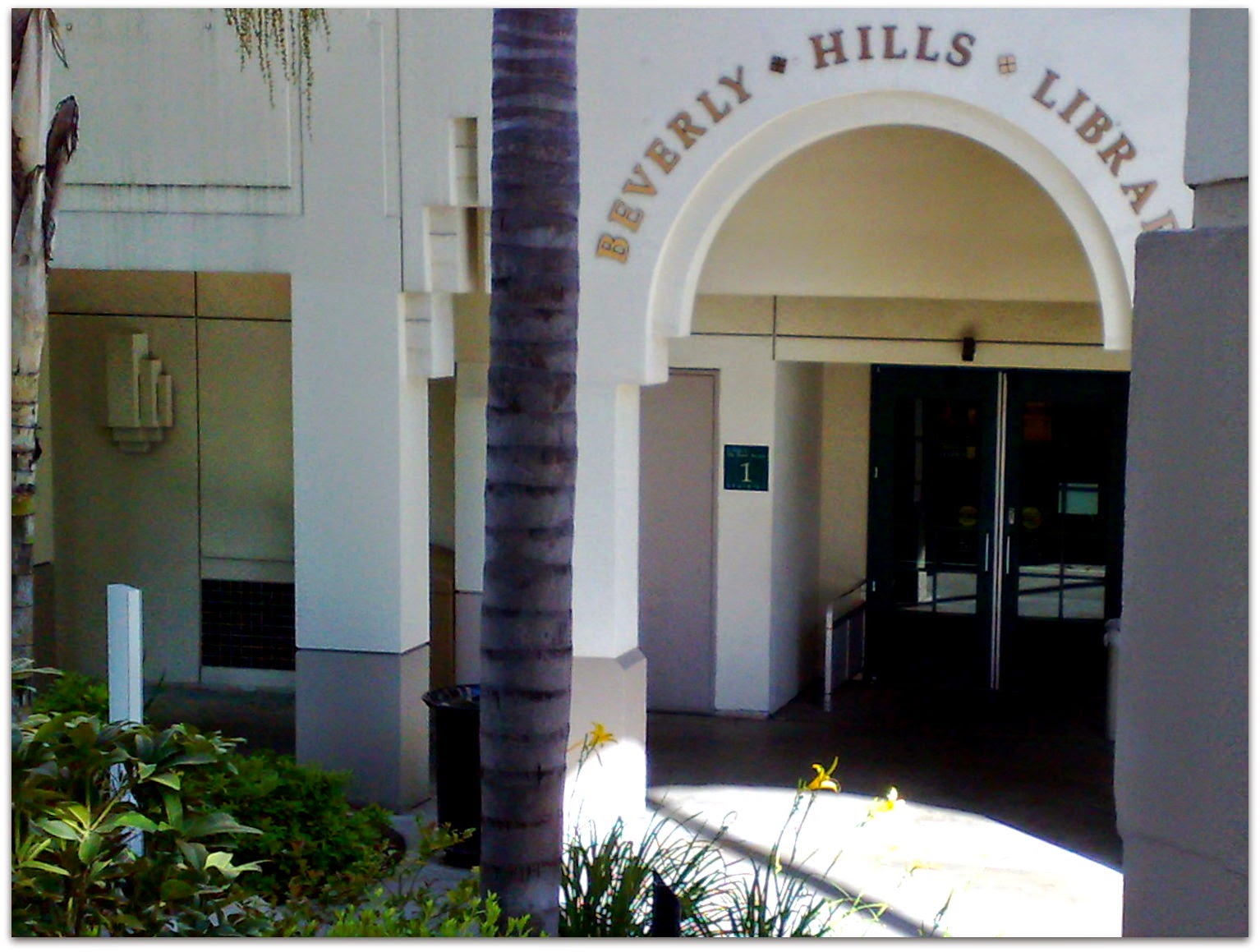 Entrance to the Beverly Hills Public Library with arched doorway, palm tree and landscaping.