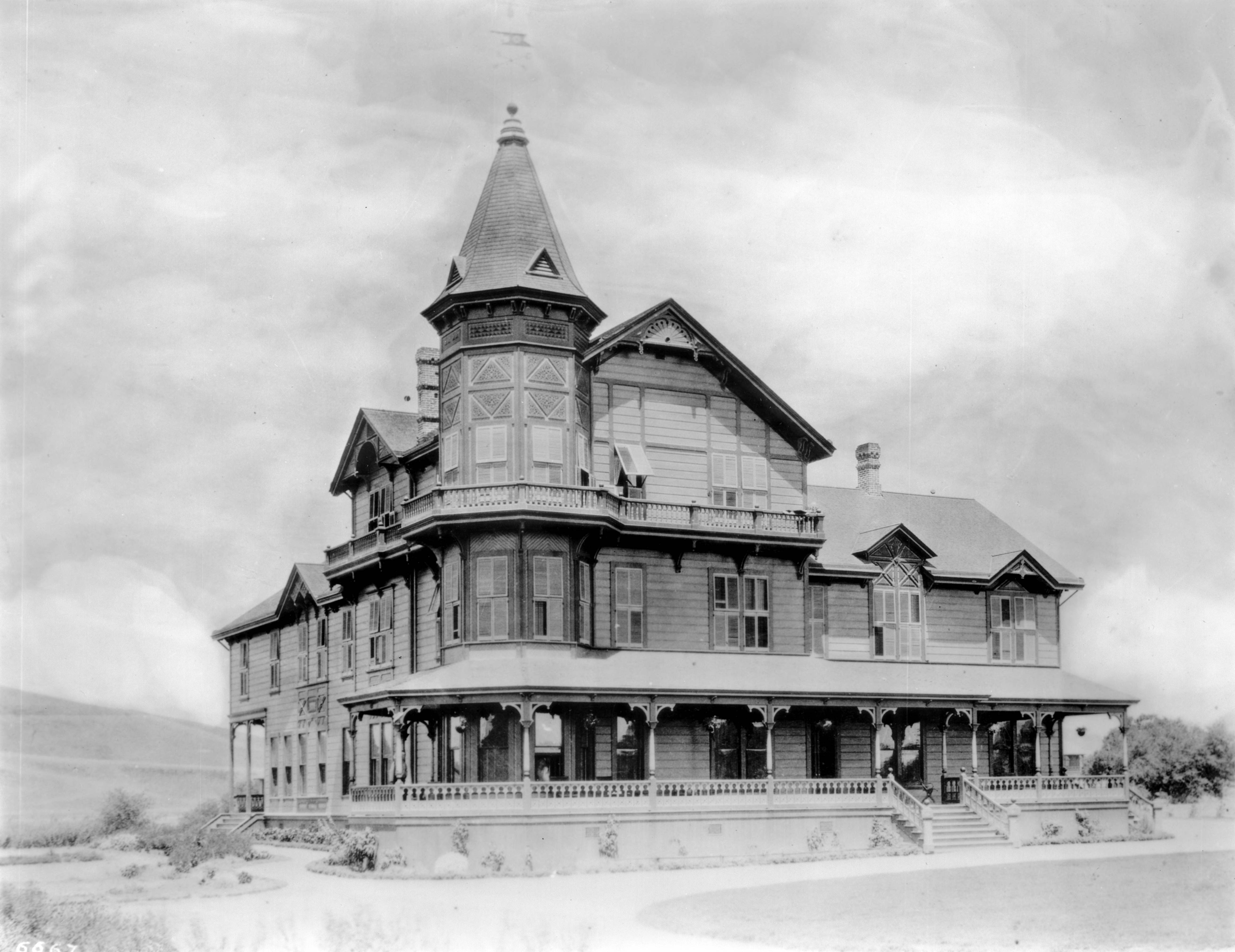 Black-and-white historic photograph of the Garvanza Hotel in Highland Park, showing a large Victorian building with a tower, wraparound porch and open land.
