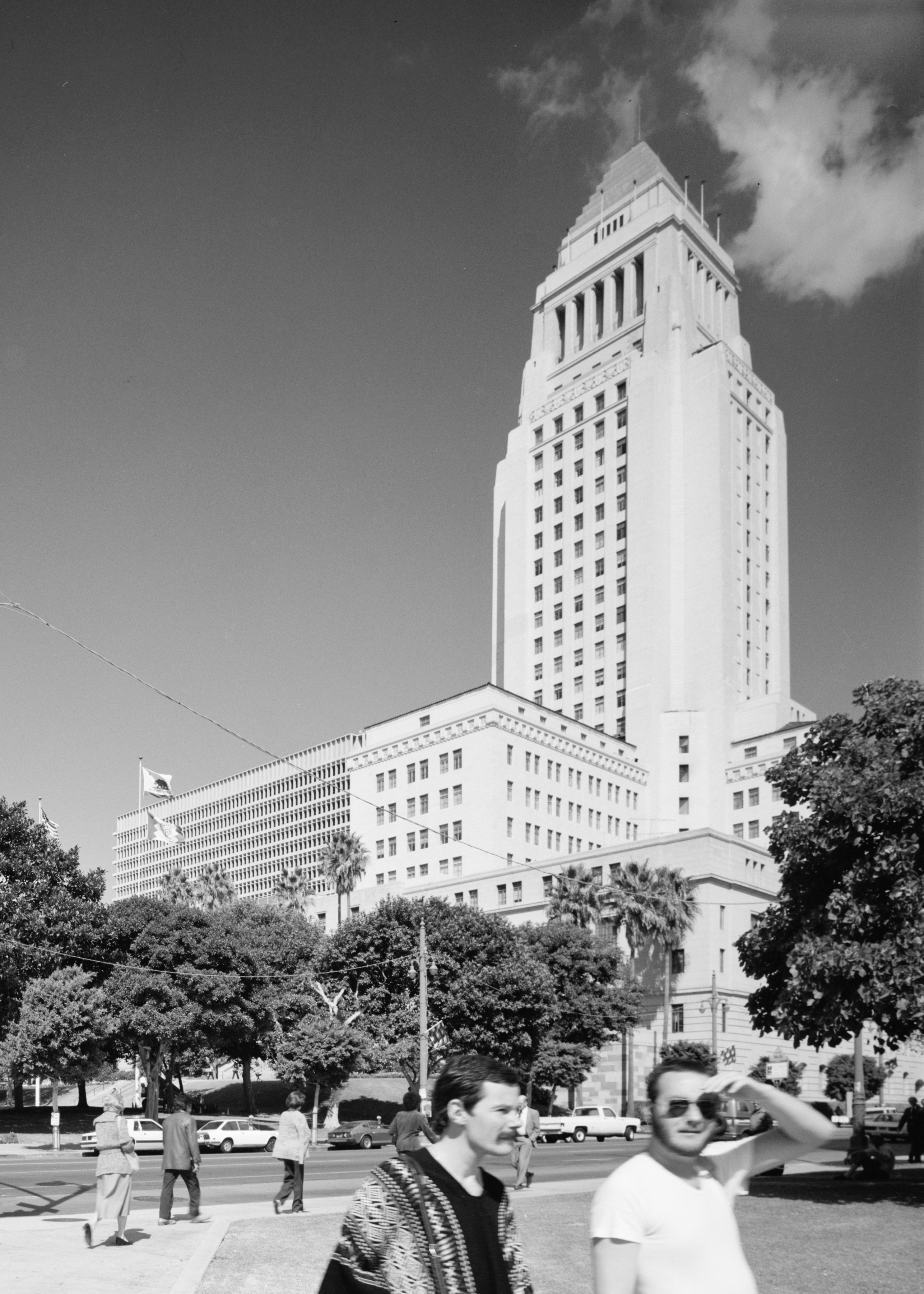 Los Angeles City Hall, one of Downtown's defining civic landmarks. Black-and-white photograph of Los Angeles City Hall rising above trees and pedestrians in Downtown Los Angeles.