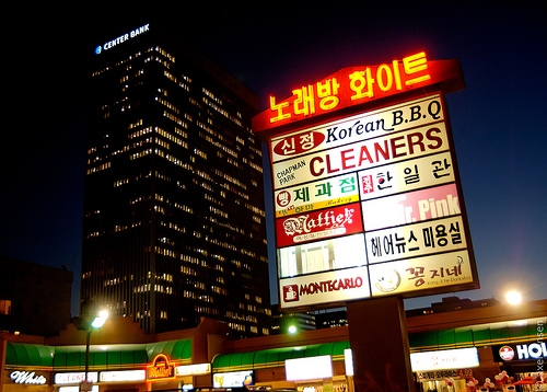 Koreatown commercial signs at night near Sixth Street and Kenmore Avenue with a high-rise building in the background.