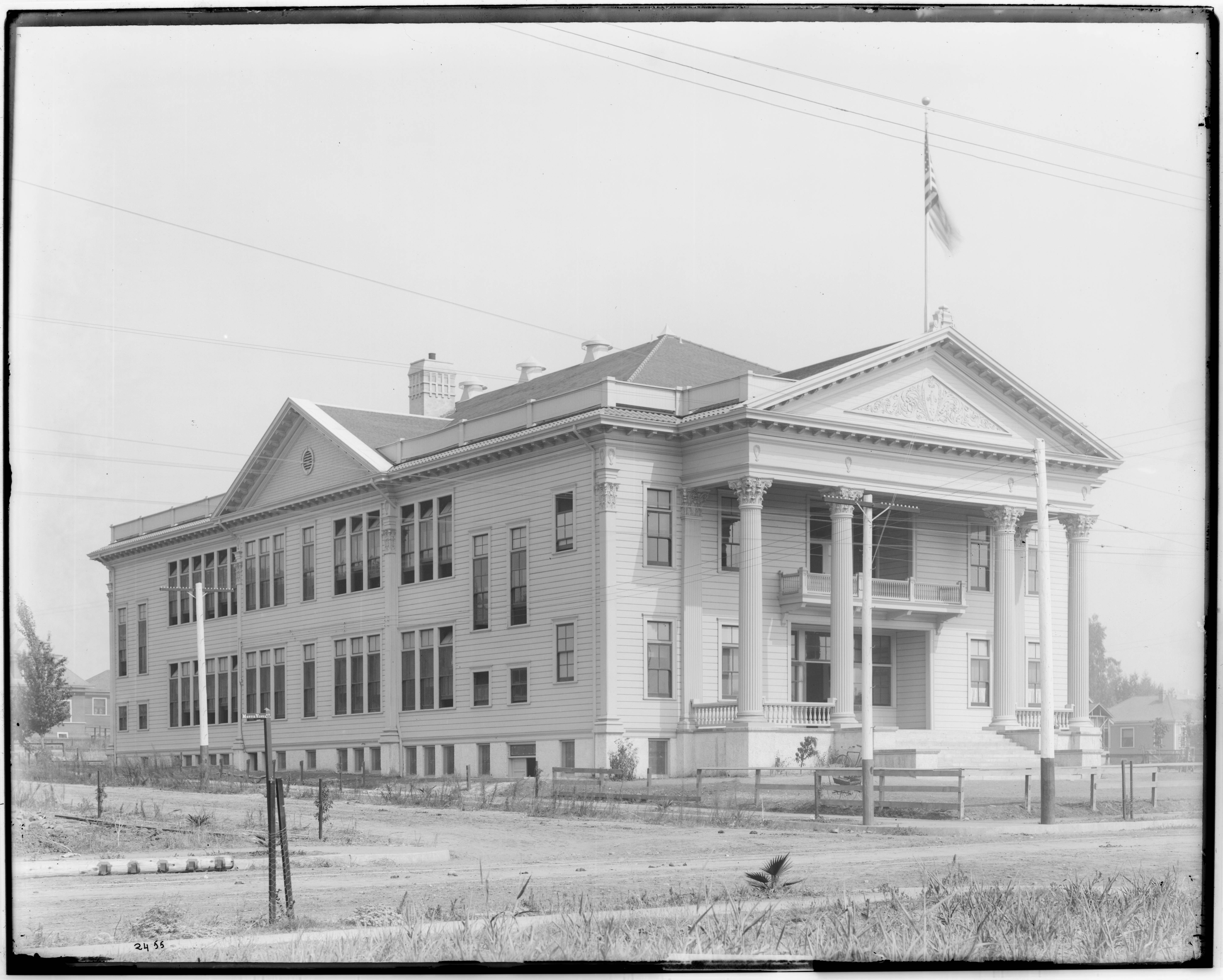 Black-and-white historic photograph of a large Classical Revival school building in Highland Park around 1905, with columns, tall windows and an American flag.