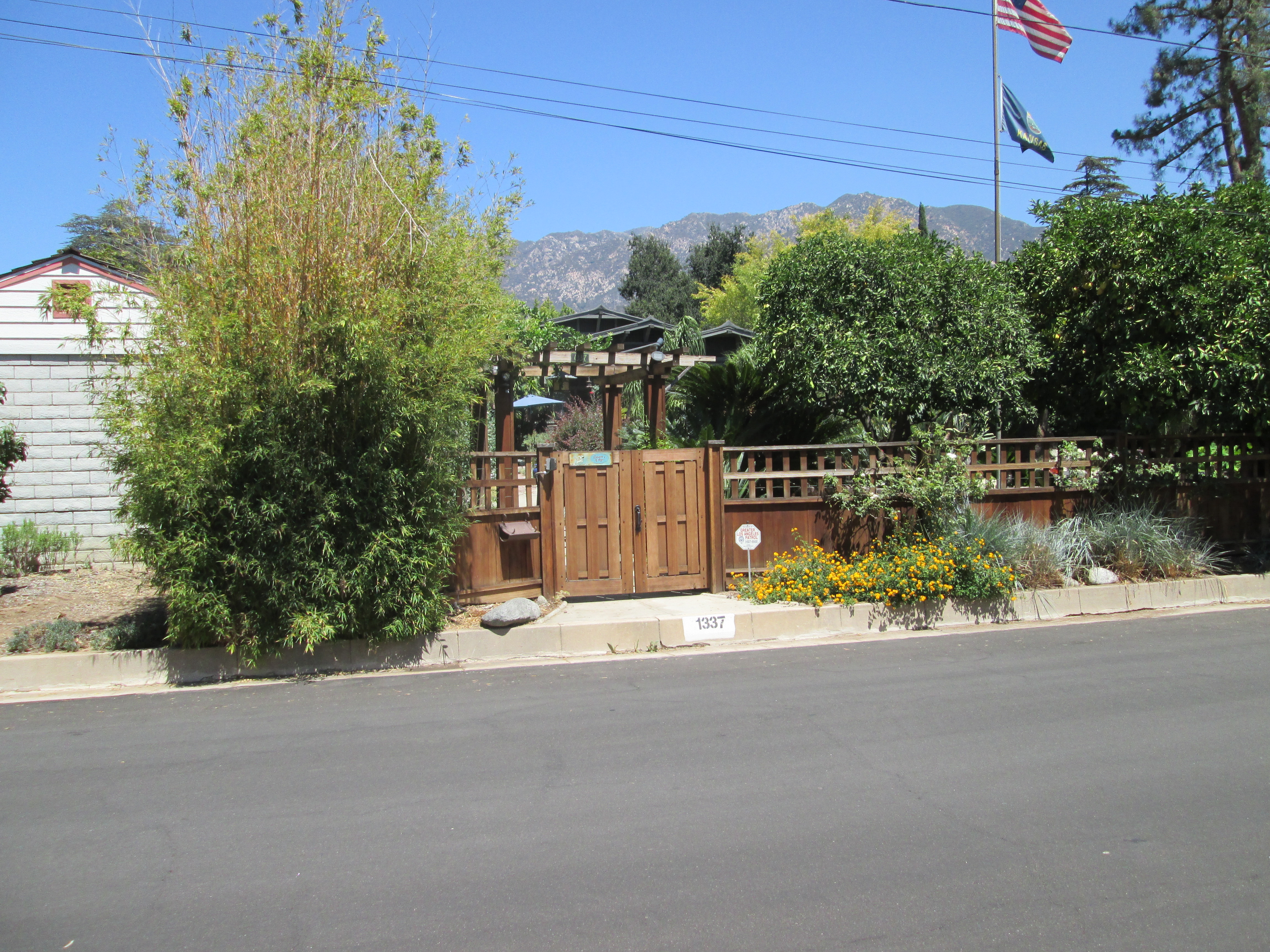 Street view of a bungalow and fenced garden in Altadena with the San Gabriel Mountains in the background.