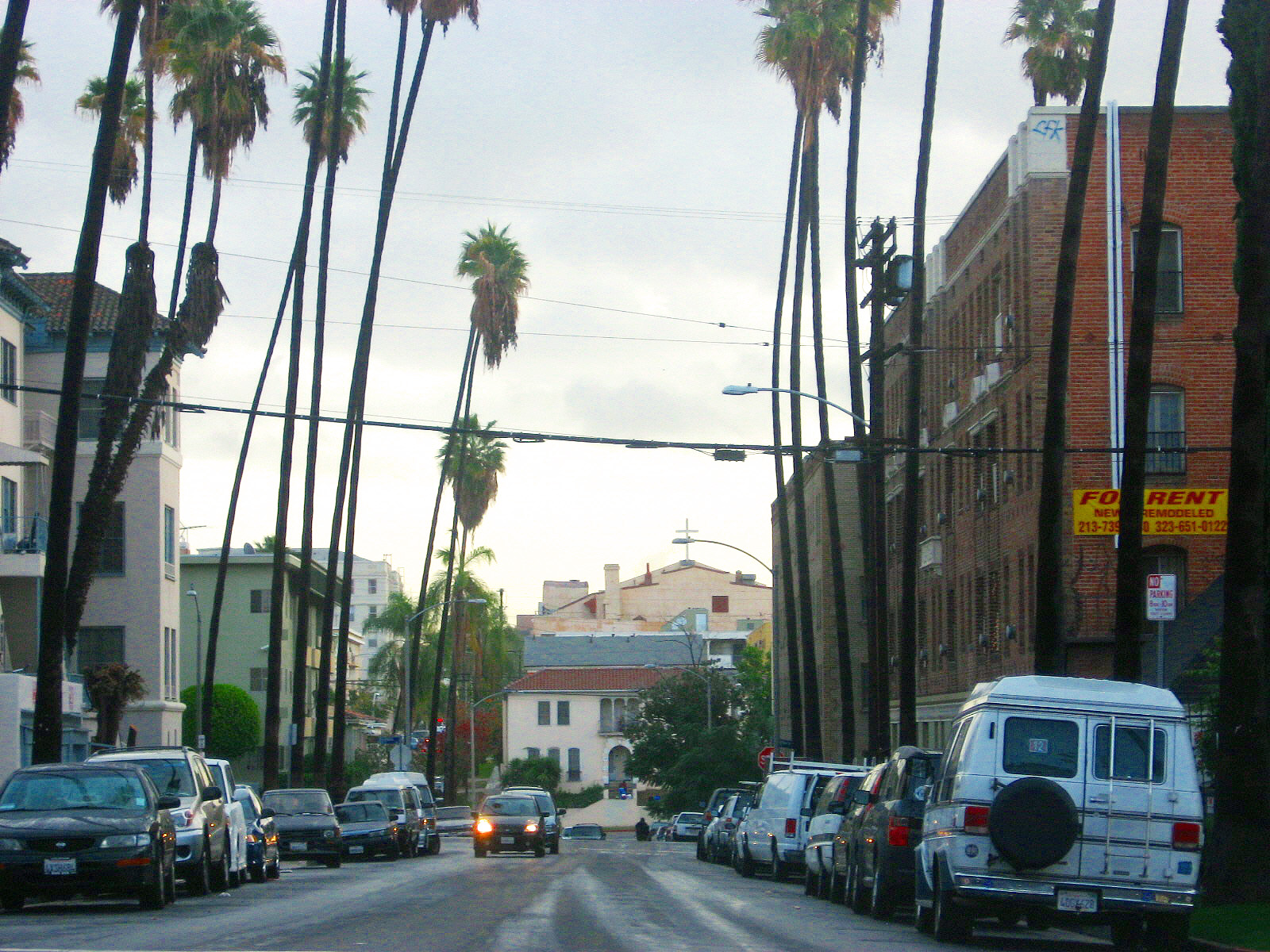 Koreatown residential street with tall palm trees, apartment buildings, parked cars and a church in the distance.