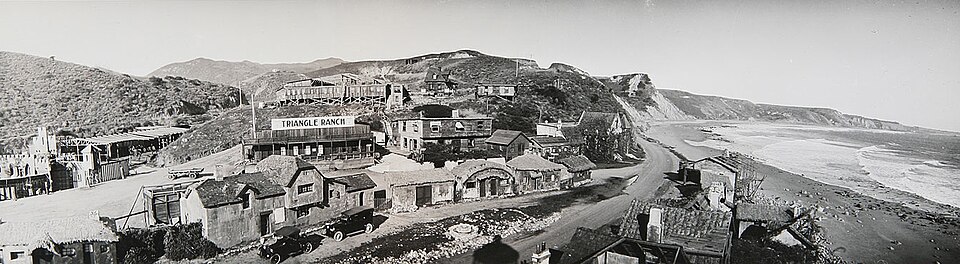 Inceville, an early silent-film backlot near what is now Pacific Palisades. Black-and-white panoramic photograph of the Inceville film backlot near Pacific Palisades, with coastal cliffs, buildings, roads and the ocean visible.