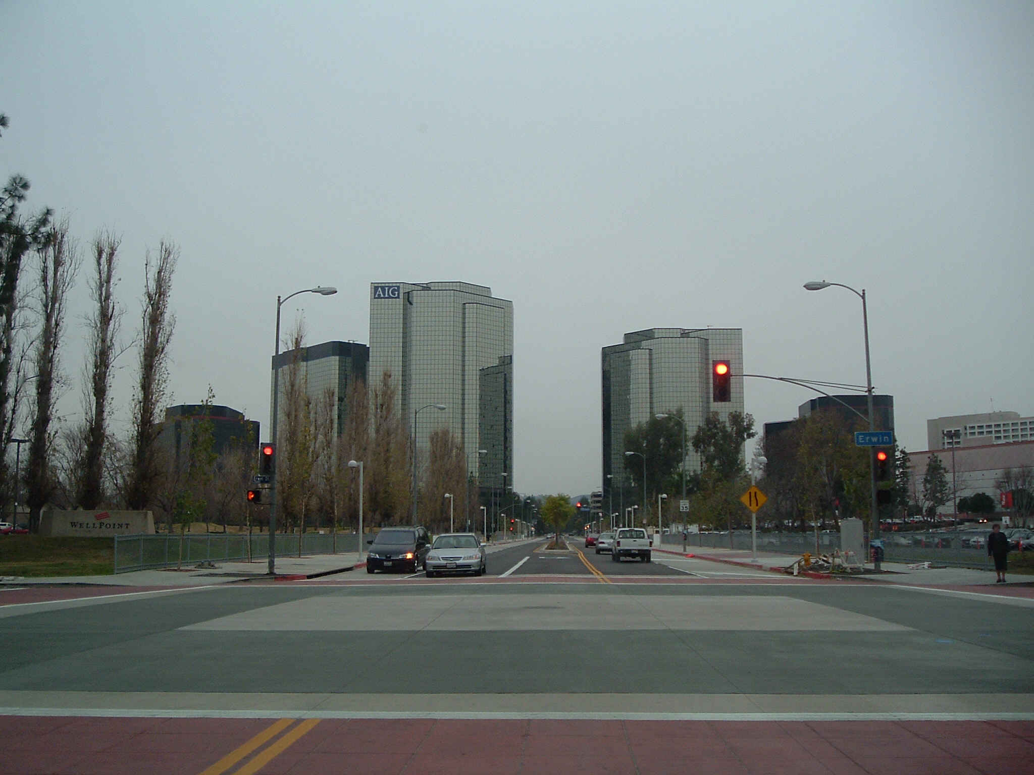 Street view of Warner Center in Woodland Hills with glass office towers, cars, traffic lights and a cloudy sky.