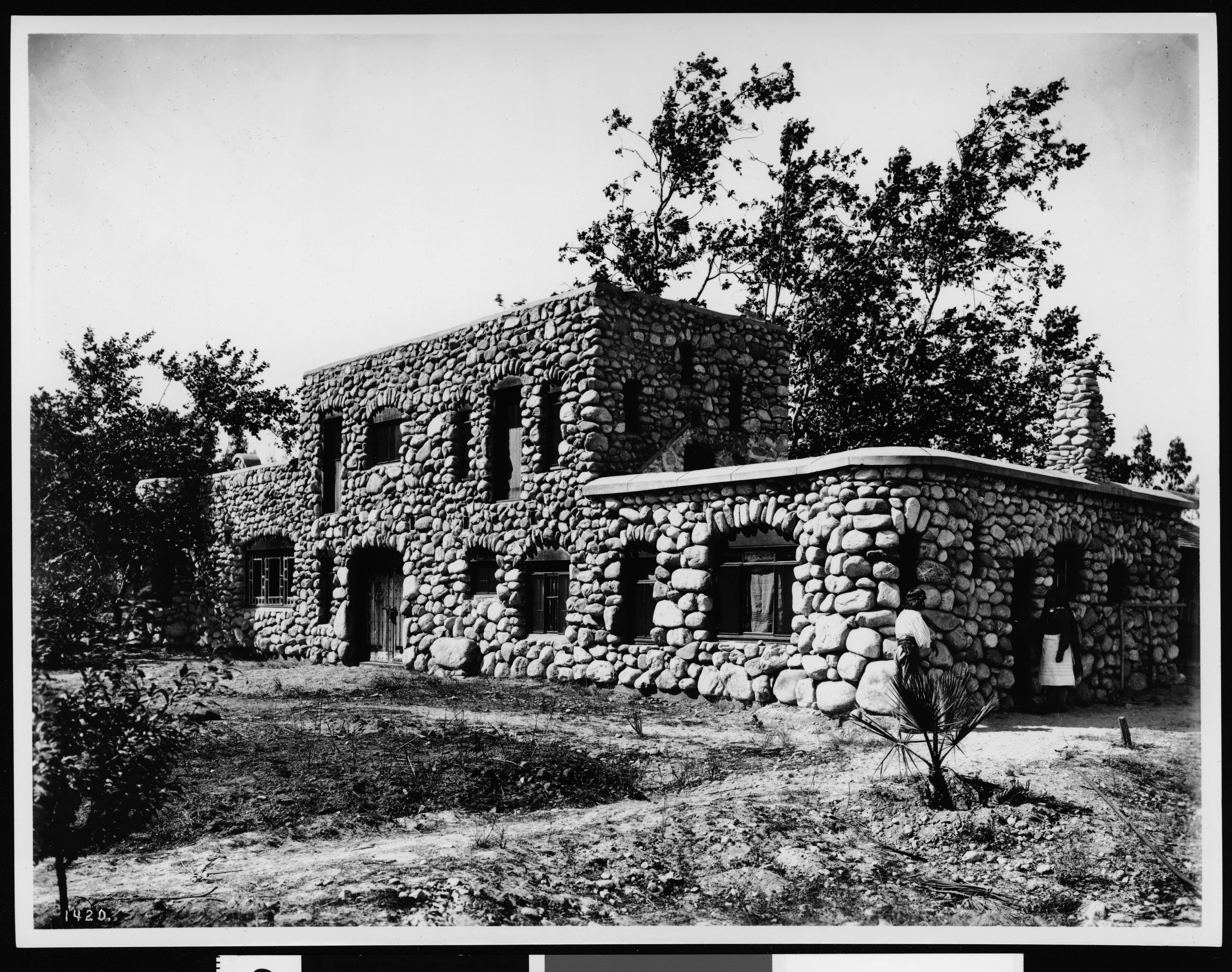 Black-and-white historic photograph of El Alisal in Highland Park, a rustic stone house built with rounded river rocks, surrounded by trees and open ground.