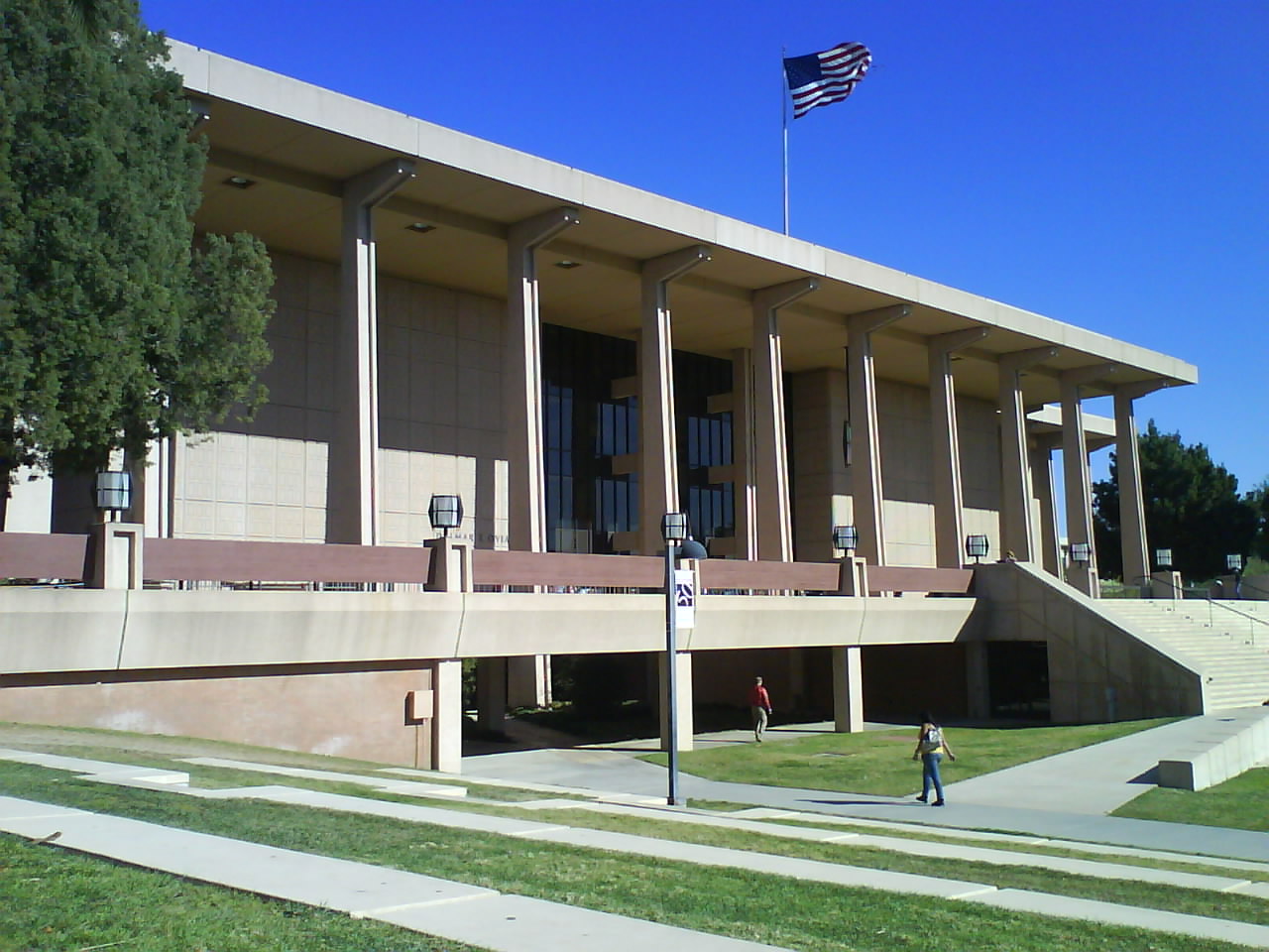 California State University Northridge library building with tall columns, a broad staircase, lawn, blue sky and an American flag.