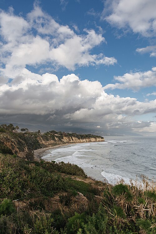 Malibu’s dramatic cliffs and coastline are part of the appeal, but they also help explain why building here can be complex. Malibu coastline near Point Dume with coastal cliffs, ocean waves, clouds, and homes along the bluff.