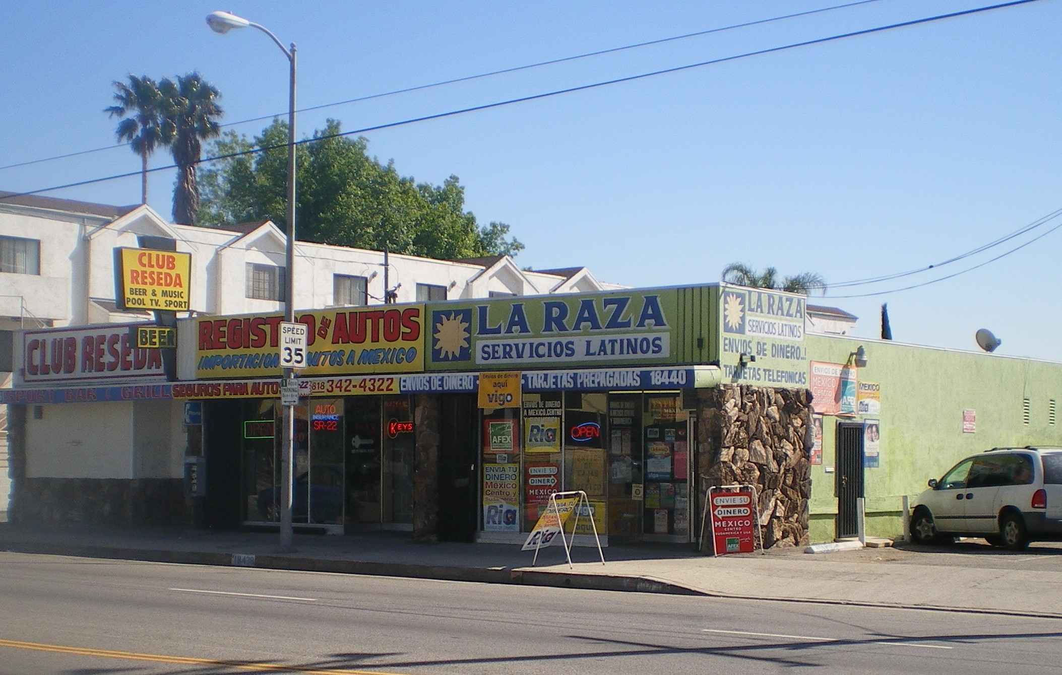 Palm-lined street in Reseda with cars, shops, neighborhood banners and a bright blue sky.