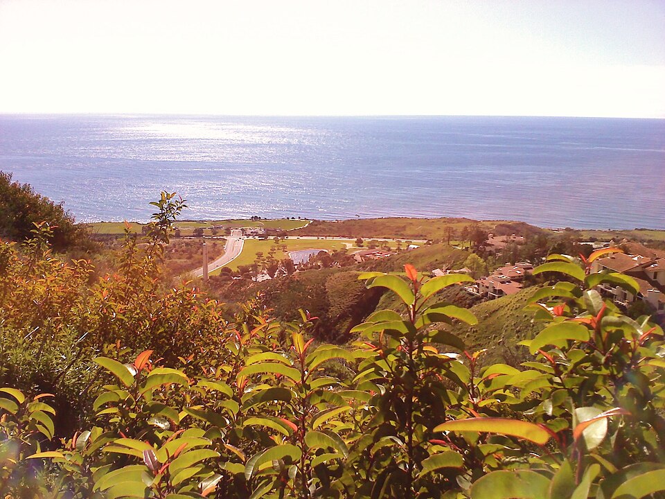 Malibu’s ocean views create extraordinary value, but the cost of creating a home here goes far beyond the purchase price of the land. Ocean view from the hills above Malibu near Pepperdine University, with green hills, homes, and the Pacific Ocean in the distance.