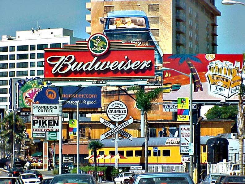 Westbound view of Sunset Boulevard on the Sunset Strip with signs, cars and palm trees.