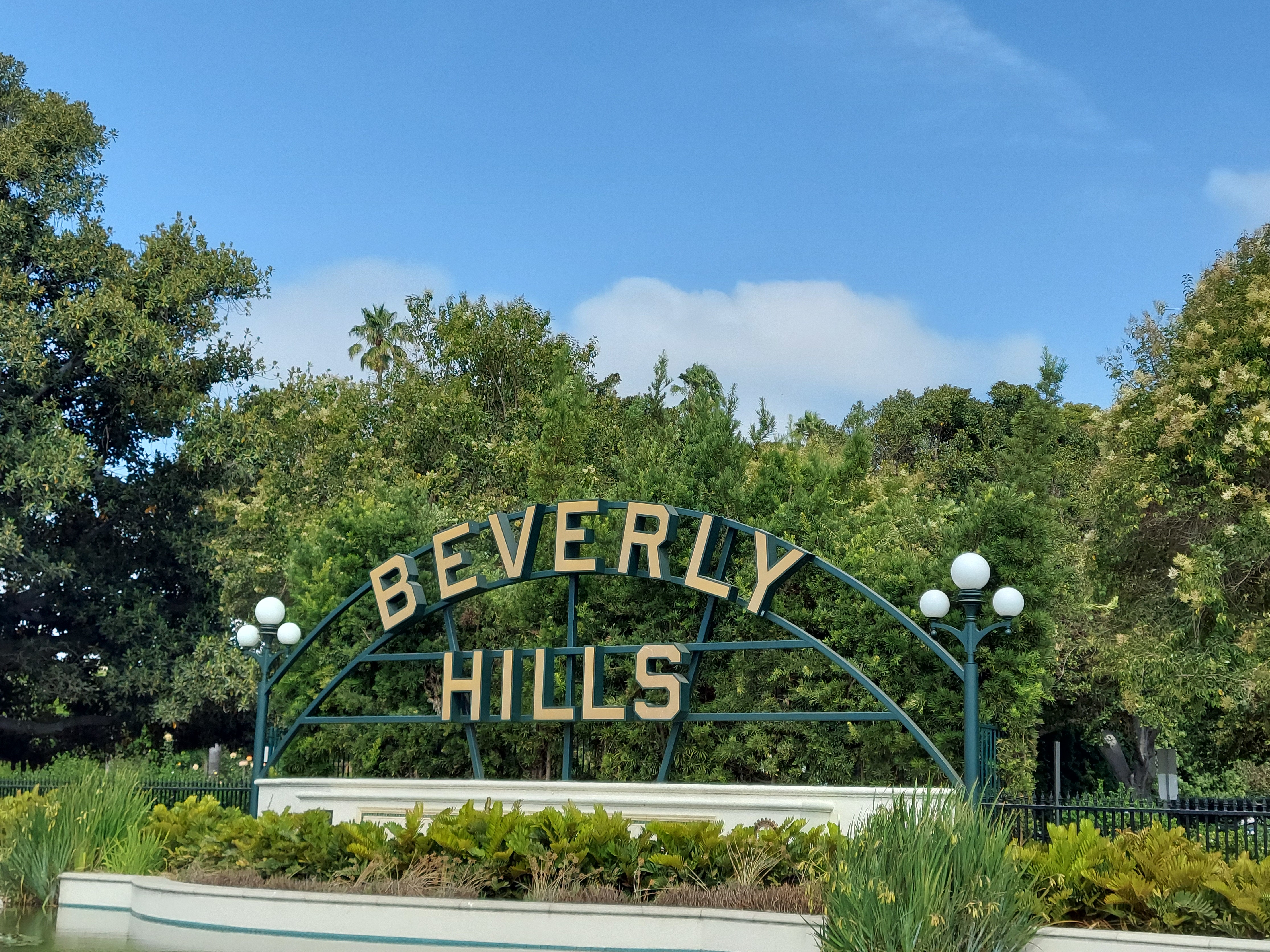 Beverly Hills sign surrounded by greenery and blue sky.