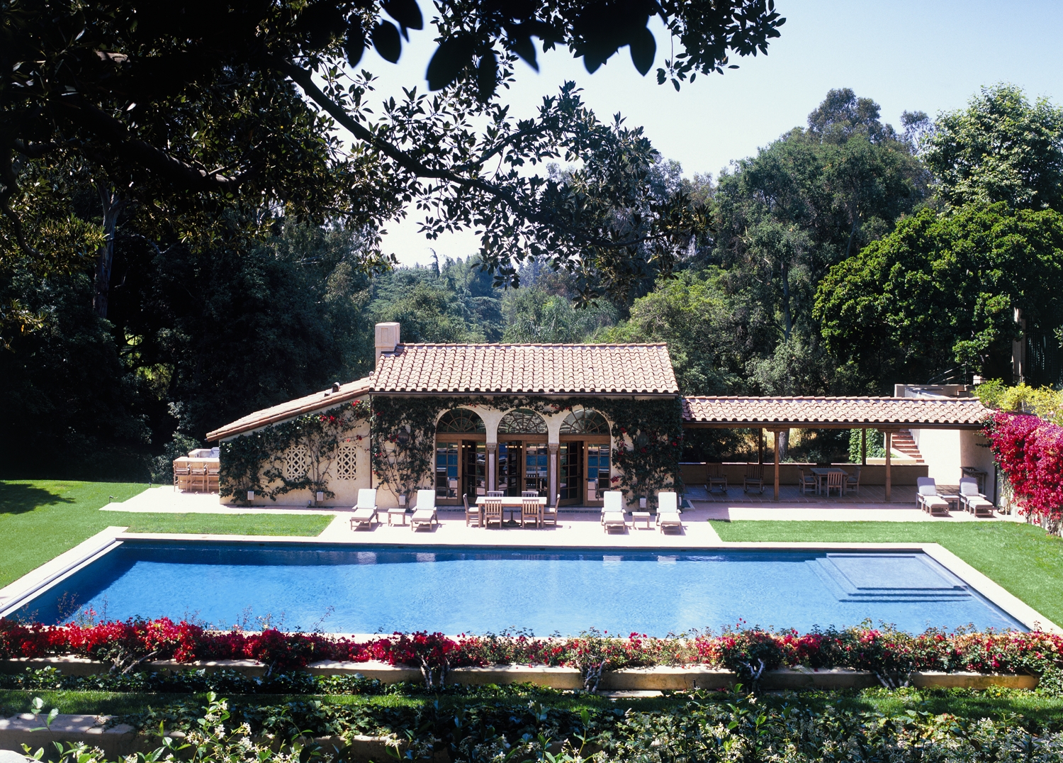 Holmby Hills pool pavilion with Spanish-style architecture, lawn and surrounding trees.