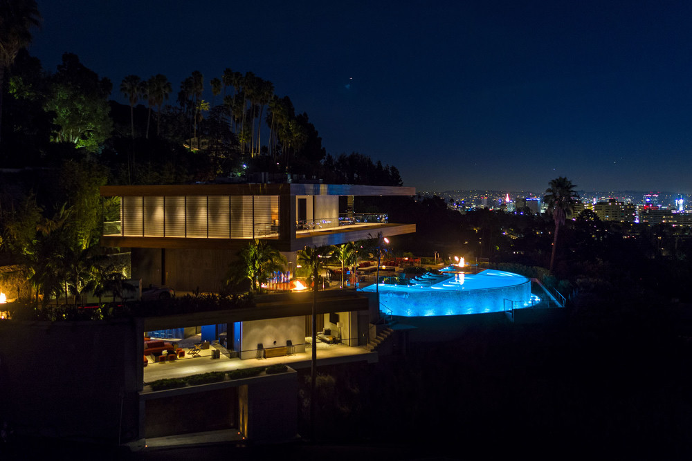 The Stanley House in Hollywood Hills Night exterior of The Stanley House above the Sunset Strip, showing its dramatic modern architecture, glowing interiors, curved pool, and panoramic Los Angeles views.