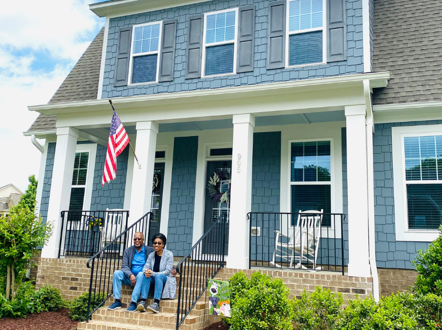 Couple sitting on front steps after they moved into new Wake Forest home, blue house with American flag