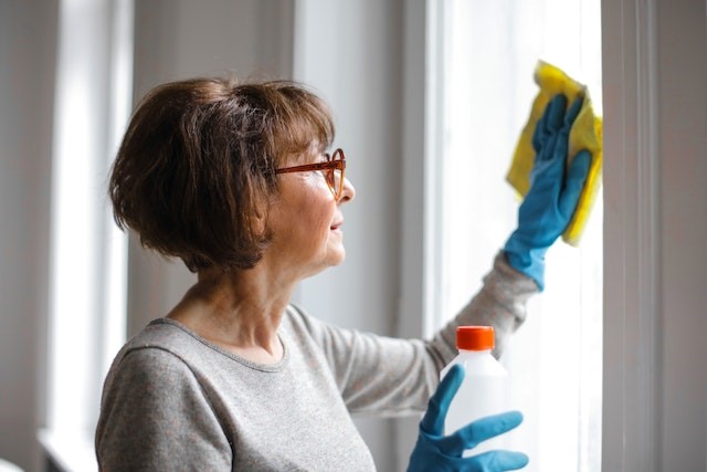 A woman cleaning windows. If you declutter your home before selling, it will be much easier to clean and maintain it