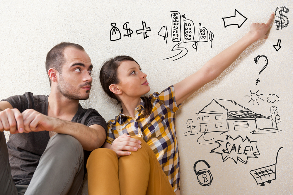man next to a women sitting pointing at a dollar sign drawn on the wall