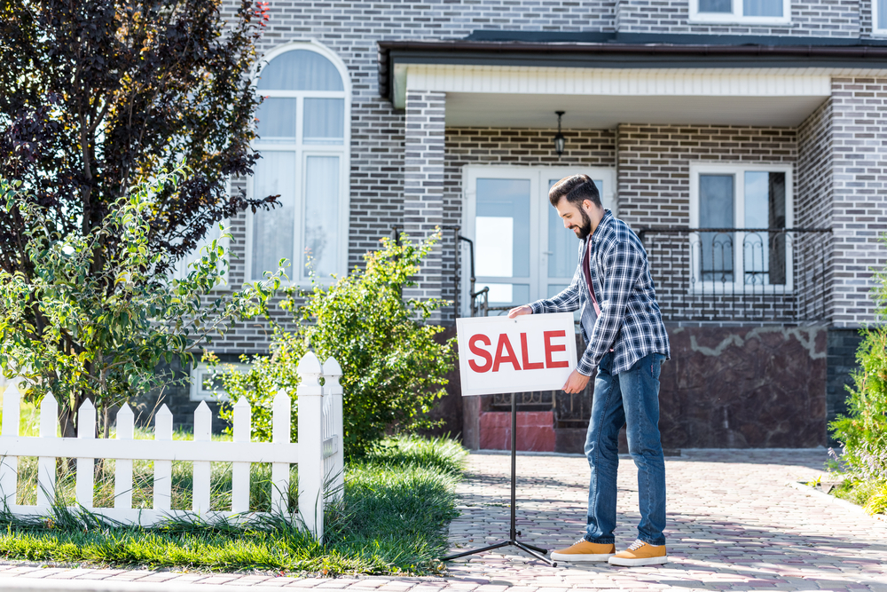 man fixing a for sale sign in front of a brick house