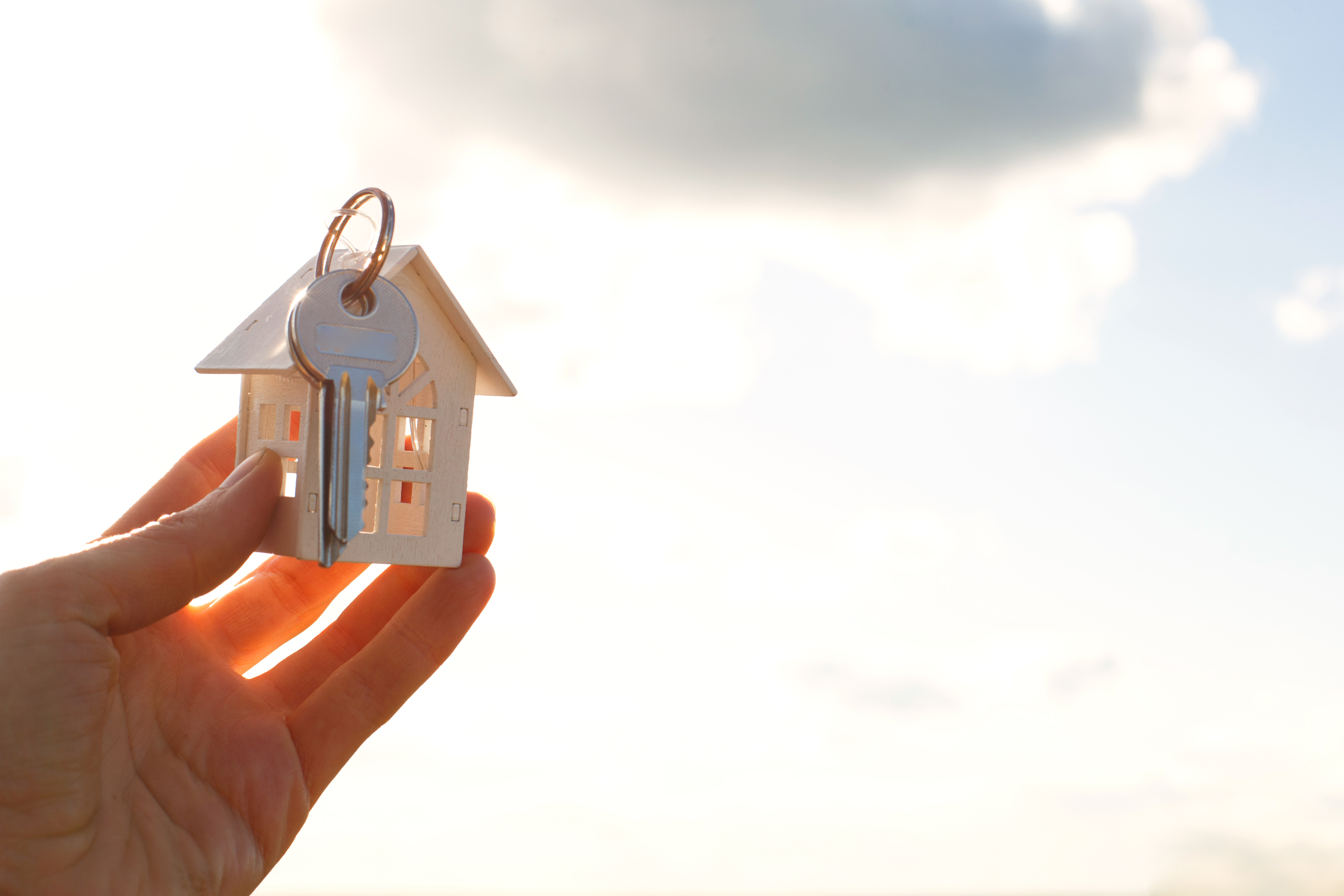 Hand presenting a house-shaped keychain and key in the warm glow of sunrise, embodying the dream of owning a home.