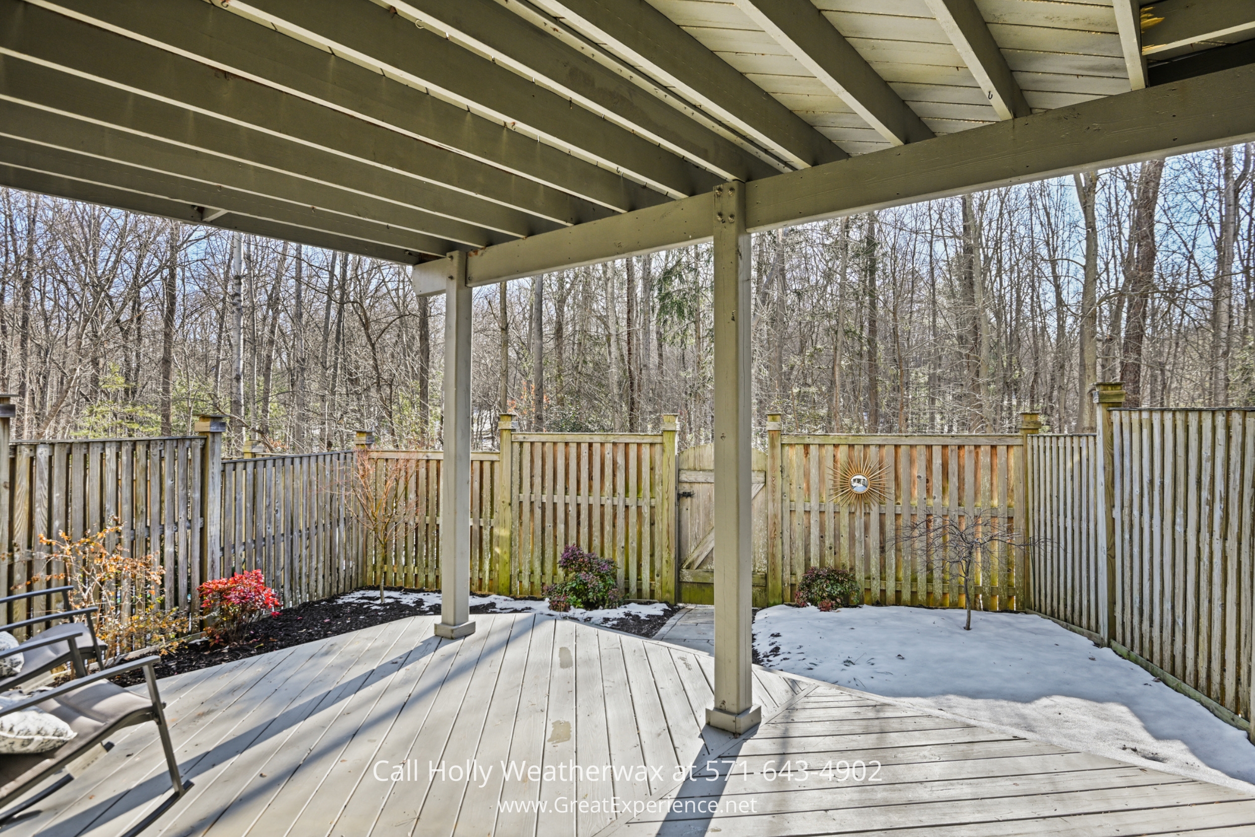 A fenced outdoor space with wooden decking, comfortable seating, and a natural backdrop of trees, offering a peaceful and private retreat.