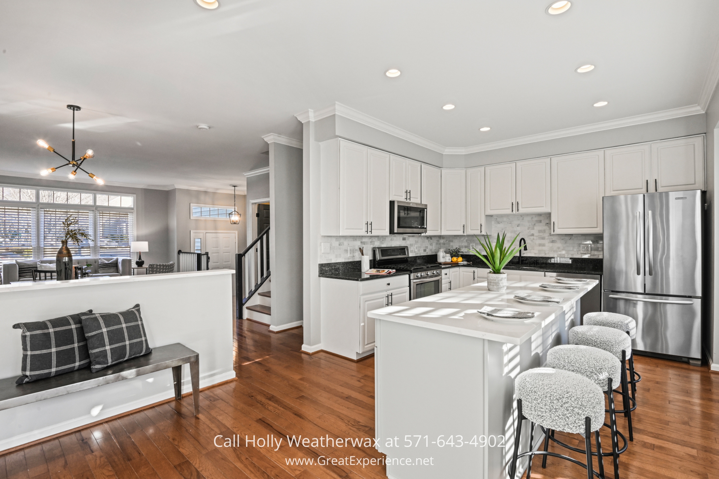 A modern white kitchen with stainless steel appliances, quartz countertops, a large island with barstool seating, and pendant lighting, perfect for cooking and entertaining.