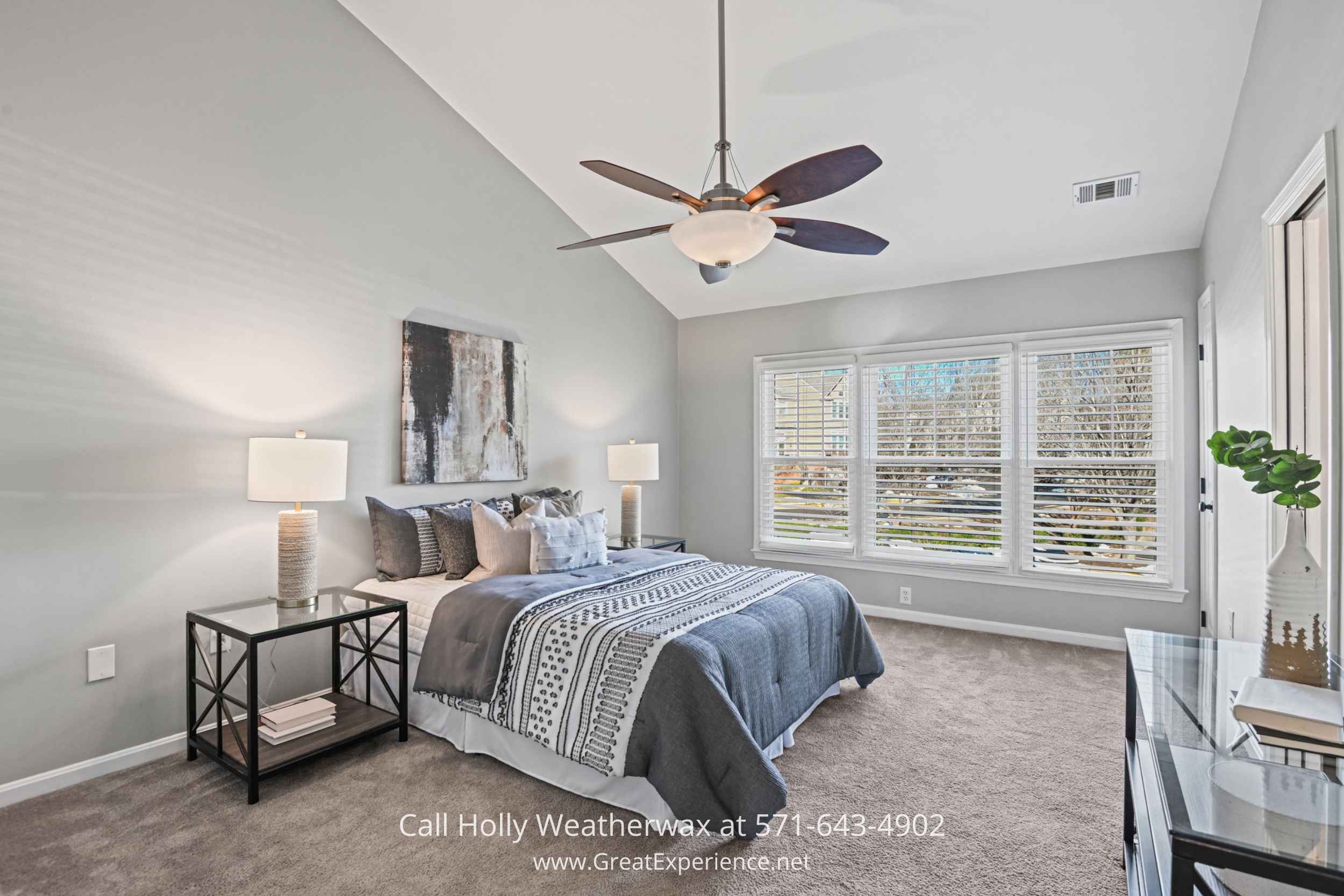 A spacious bedroom with a vaulted ceiling, a king-sized bed with stylish bedding, large windows with white blinds, and neutral decor creating a calming atmosphere.