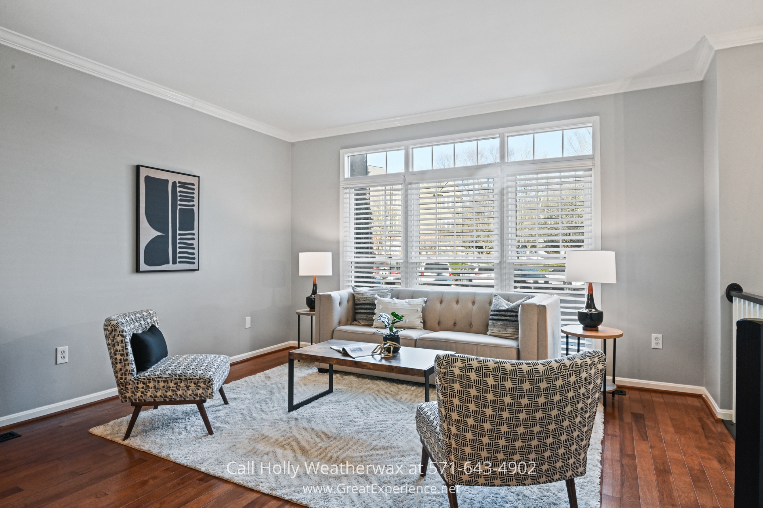 A spacious living room with a large front window, a neutral gray couch, stylish patterned chairs, and contemporary artwork, creating a cozy and elegant space.