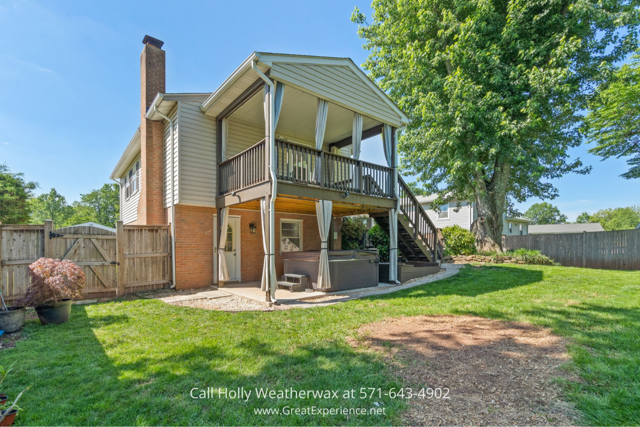 Backyard view of a covered deck with stairs and lower patio, surrounded by a spacious lawn in this Chantilly VA home for sale.