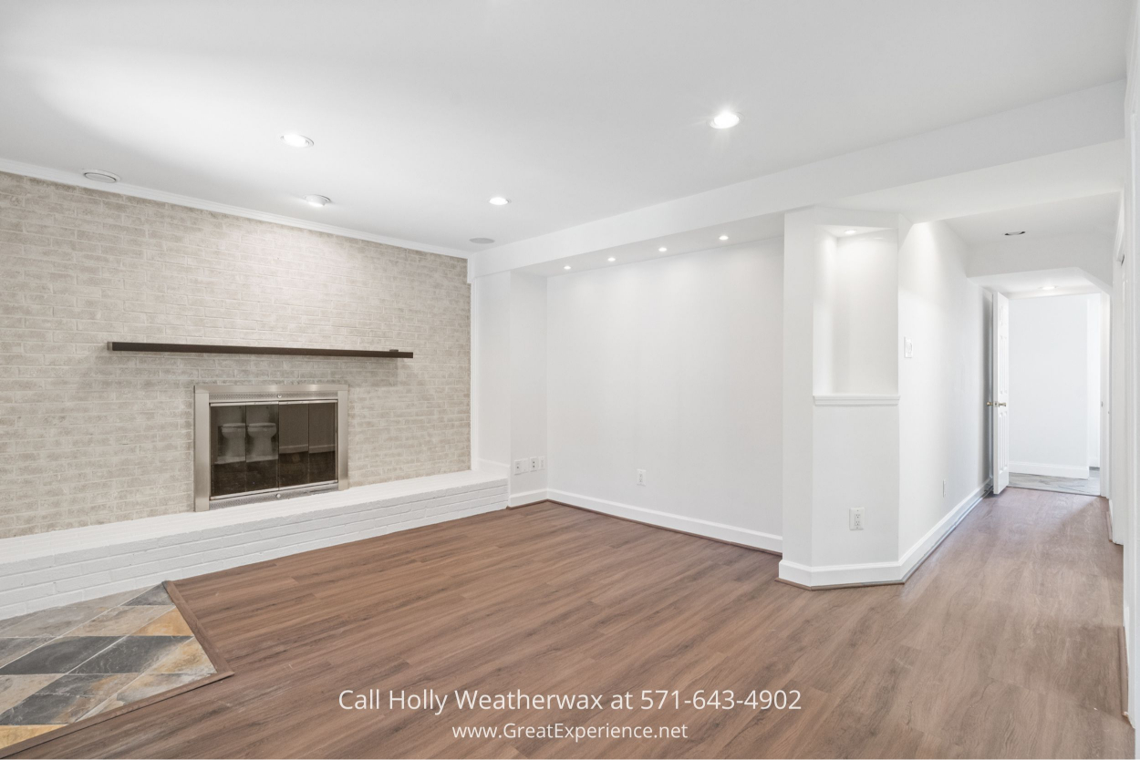 Open family room featuring a modern white brick fireplace and rich wood-look floors in this Chantilly VA home for sale.