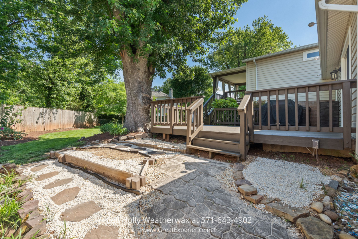 Landscaped backyard with stone pathways, gravel accents, and wooden steps leading to a charming rear deck in this Chantilly VA home for sale.